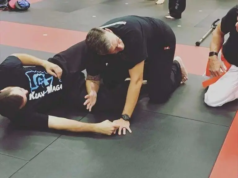 Instructor demonstrates wrist control and ground defense technique during an adult Krav Maga self-defense session.
